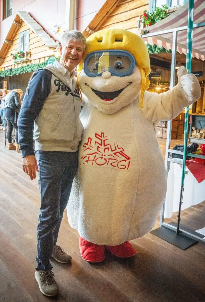 Mascotte Schörgi van Filzmoos met skihelm en skibril steekt zijn duim op