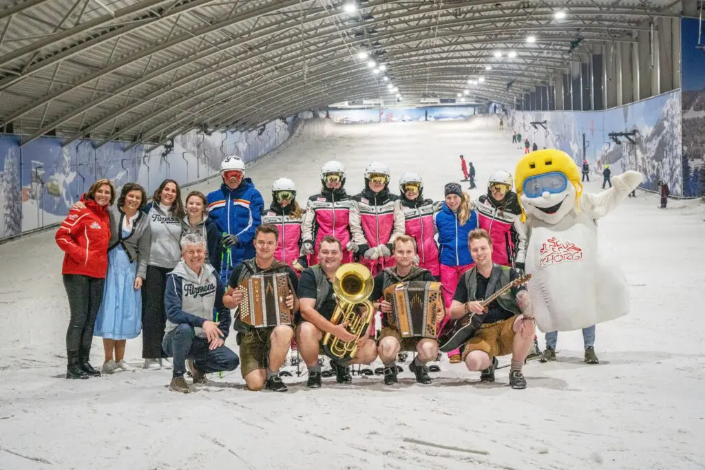 Groep uit Filzmoos met muzikanten in lederhosen, skileraren en mascotte Schörgi op de piste van SnowWorld Amsterdam