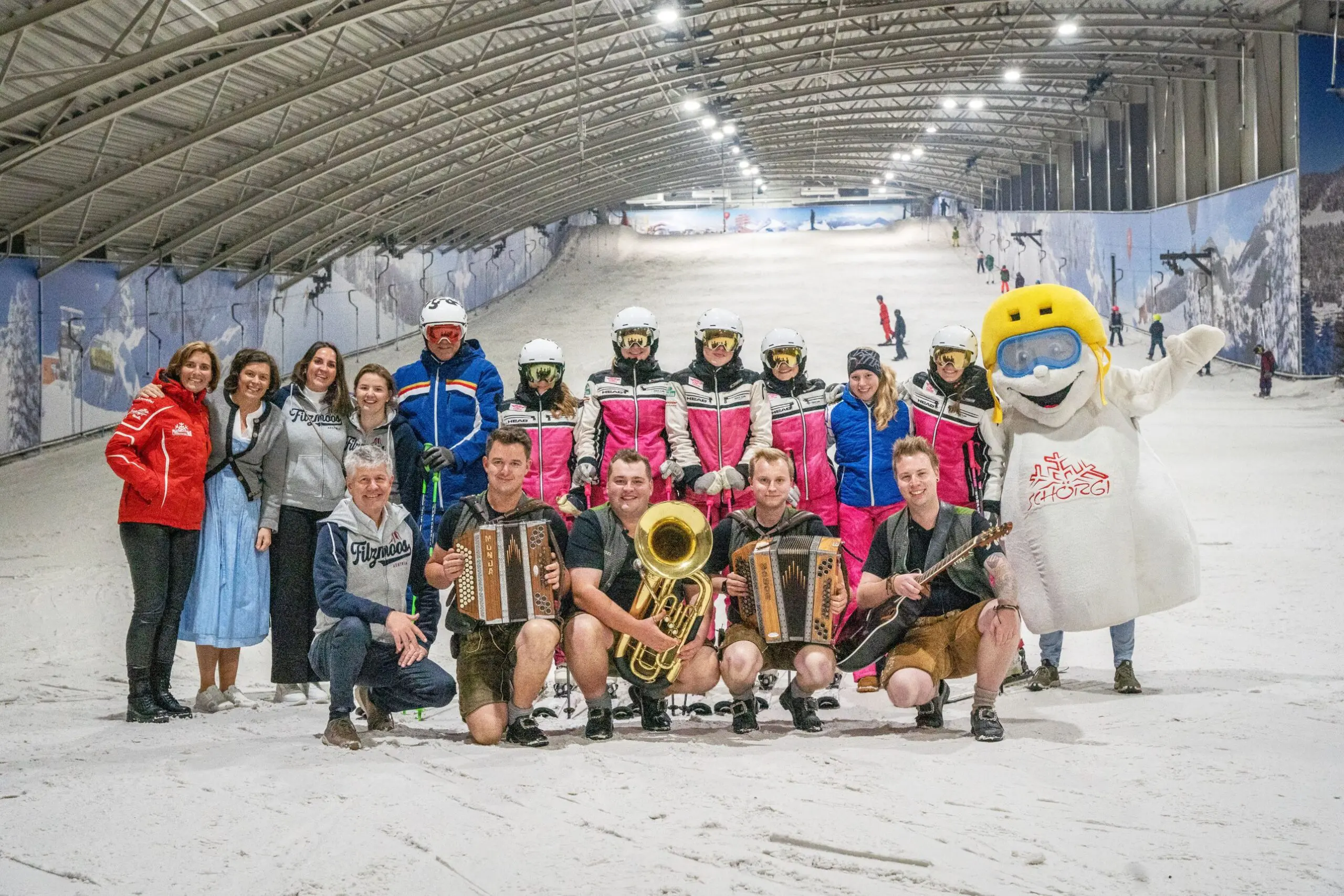 Groep uit Filzmoos met muzikanten in lederhosen, skileraren en mascotte Schörgi op de piste van SnowWorld Amsterdam
