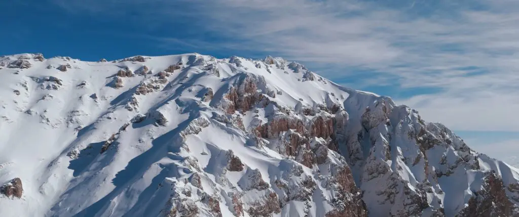 Besneeuwde bergwand in de Chimgan-bergen in Oezbekistan onder een blauwe lucht